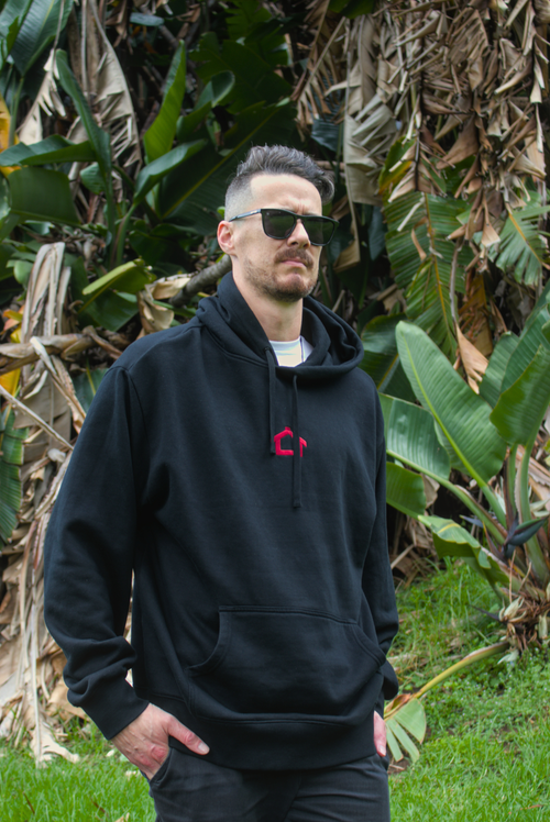 Man wearing a black hoodie with a red logo in a natural setting