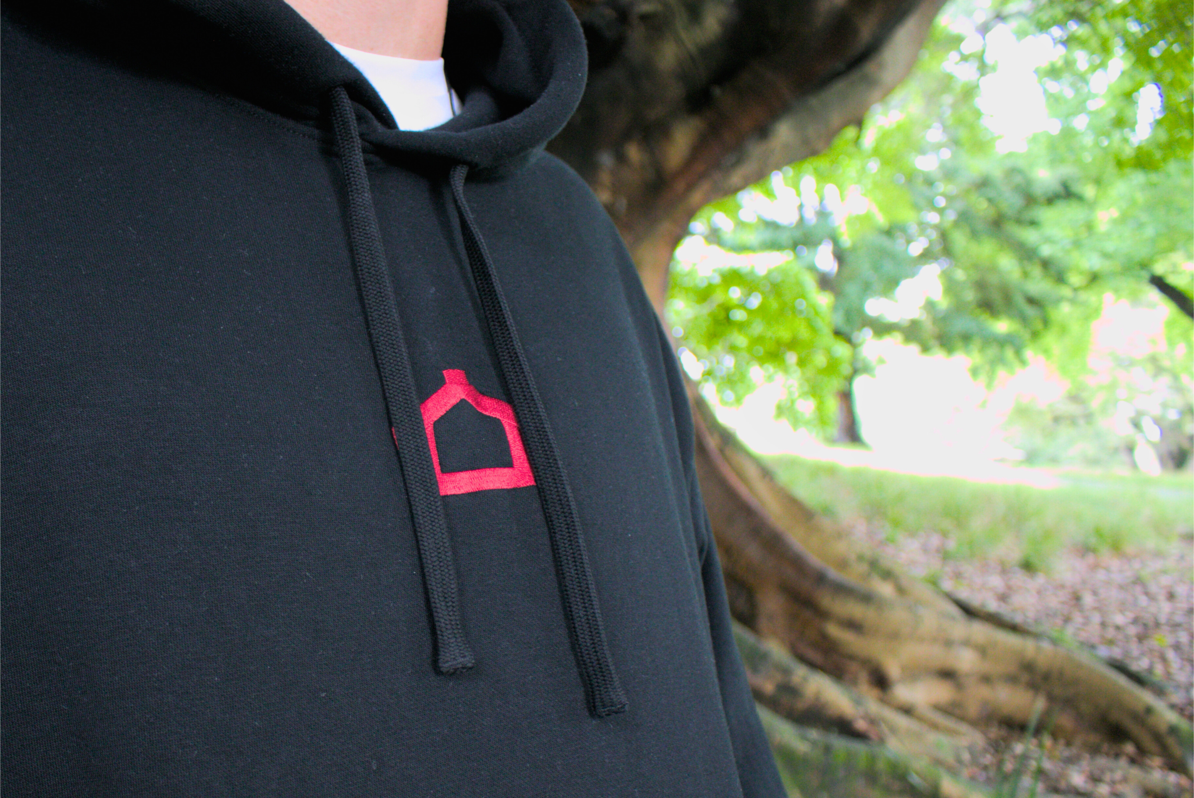 Person wearing a black hoodie with a red logo in a park setting